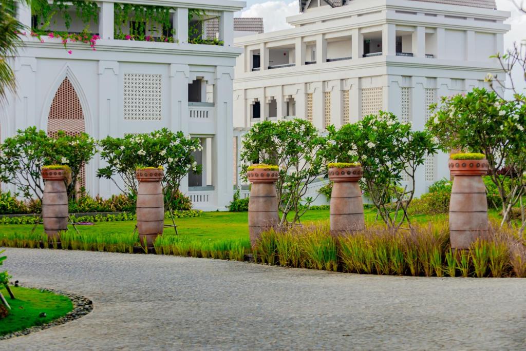 Dārza ainava ar elegantiem baltiem ēkām un dekoratīvām puķu podiem, kas rotā ceļu, izveidojot mierīgu un estētisku atmosfēru.