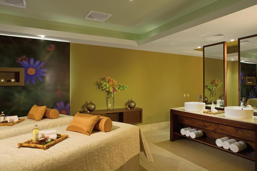 Spa telpa ar divām masāžas gultām, dekoratīvām akcentu detaļām un mūsdienīgu vannas istabas zonu. Svaigi ziedi un relaksējoša atmosfēra veido ideālu vidi atpūtai.