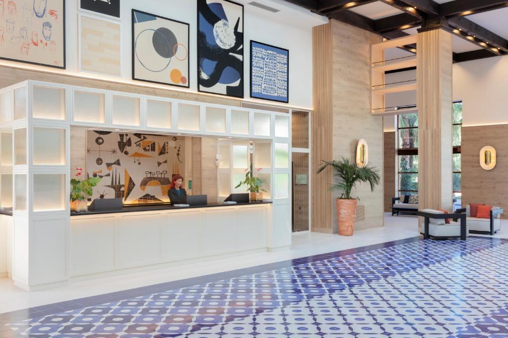 Mūsdienīgs viesnīcas reģistratūras interjers ar mākslas darbiem uz sienām un elegantu flīžu grīdu. Siltas krāsas un augi piešķir patīkamu atmosfēru.