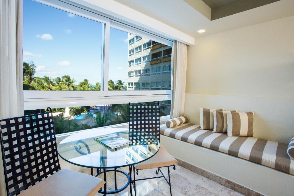 Mūsdienīga viesnīcas istaba ar ērtu sēdvietu, stikla galdu un skatu uz dabu. Gaismas pieplūdums un mūsdienīgs dizains rada relaksējošu atmosfēru.