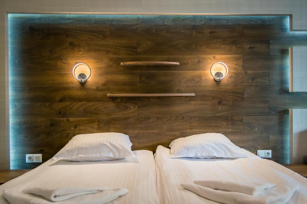 Mūsdienīgs guļamistabas interjers ar divguļamo gultu, koka sienu un stilīgām gaismas ķermeņiem. Izcila dizaina elementi rada siltu un viesmīlīgu atmosfēru.