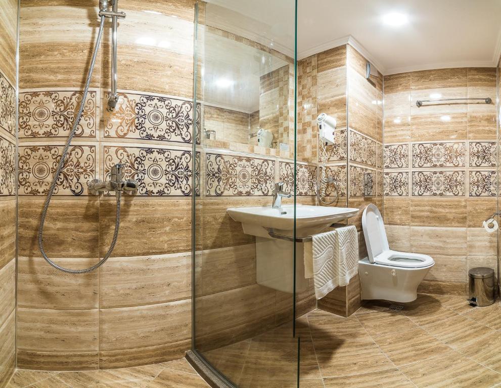 Mūsdienīgs vannas istabas interjers ar stikla dušas kabīni, elegantām flīzēm un balto sanitāriju, izceļot siltas krāsas un stilīgu dizainu.