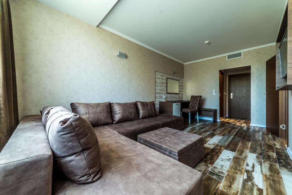 Mūsdienīgs viesnīcas numurs ar brūnu dīvānu, krēslu un galdu, kas nodrošina ērtu atpūtu. Telpa ir gaiša ar koka grīdu un neitrālām sienām.