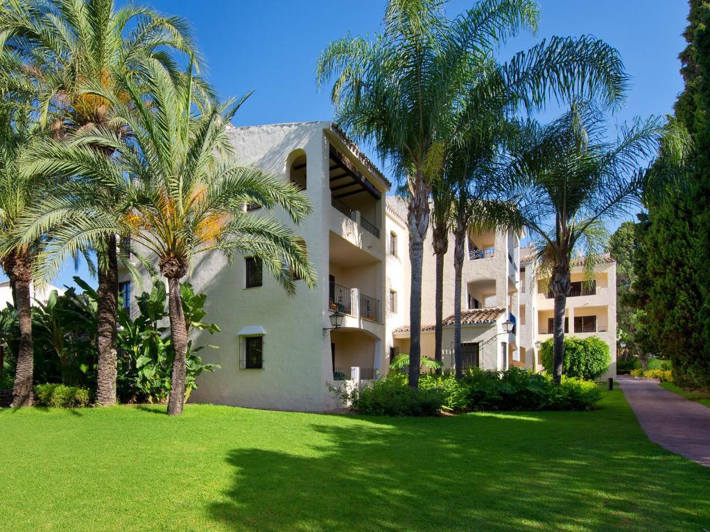 Vasaras atpūtas vieta ar tropiskām palmām un viesnīcas ēkām, ieskauta zaļajā zālē. Ideāla vide relaksācijai un atpūtai.