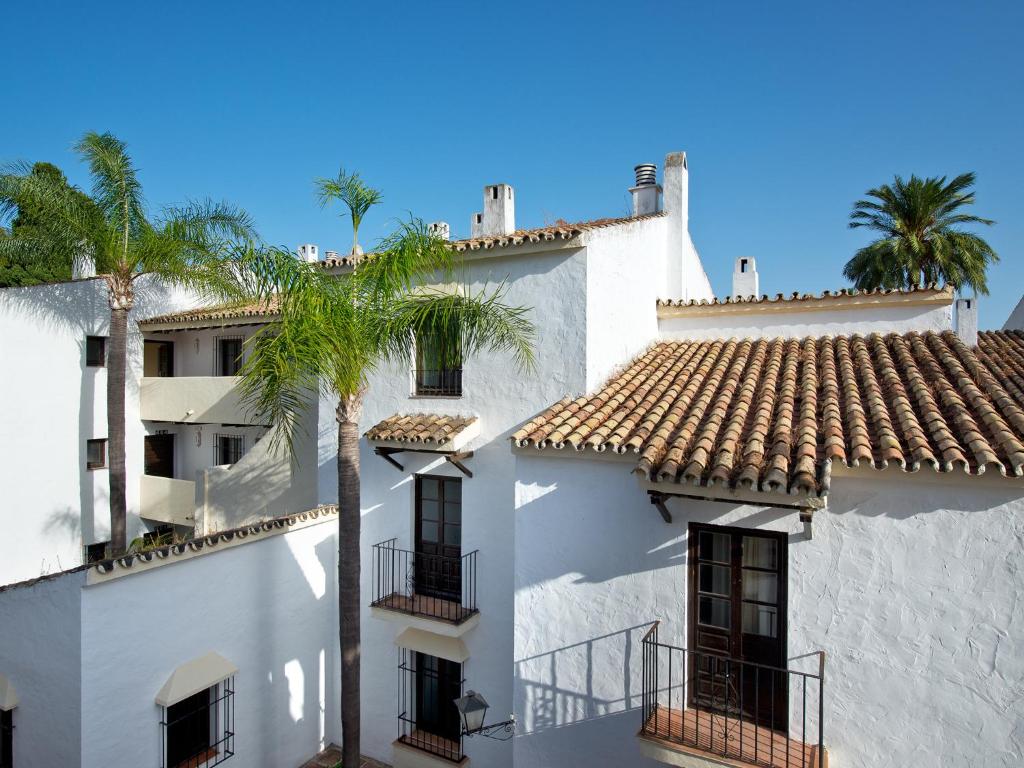 Baldakins ar baltiem ēku fasādēm, jumtiem ar flīzēm un palmām zem skaidras debess.