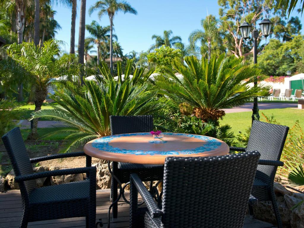 Dārza galds ar četrām krēsliem, ieskauts zaļojošām palmām un ziediem, radot mierīgu un relaksējošu atmosfēru. Ideāla vieta atpūtai un socializēšanai.