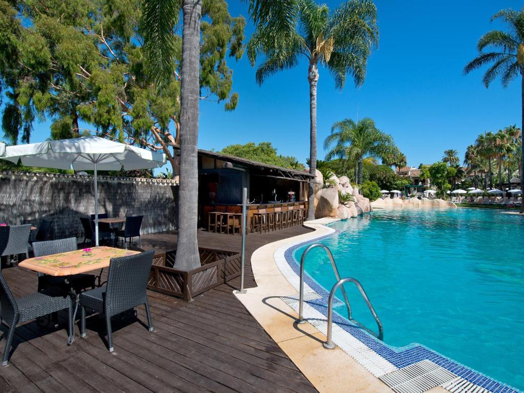 Peldbaseins ar skatu uz palmām un terasi, kurā ir galdi un krēsli, ideāli piemērots atpūtai. Viegla atmosfēra un saulains laiks rada lielisku vidi relaksācijai.