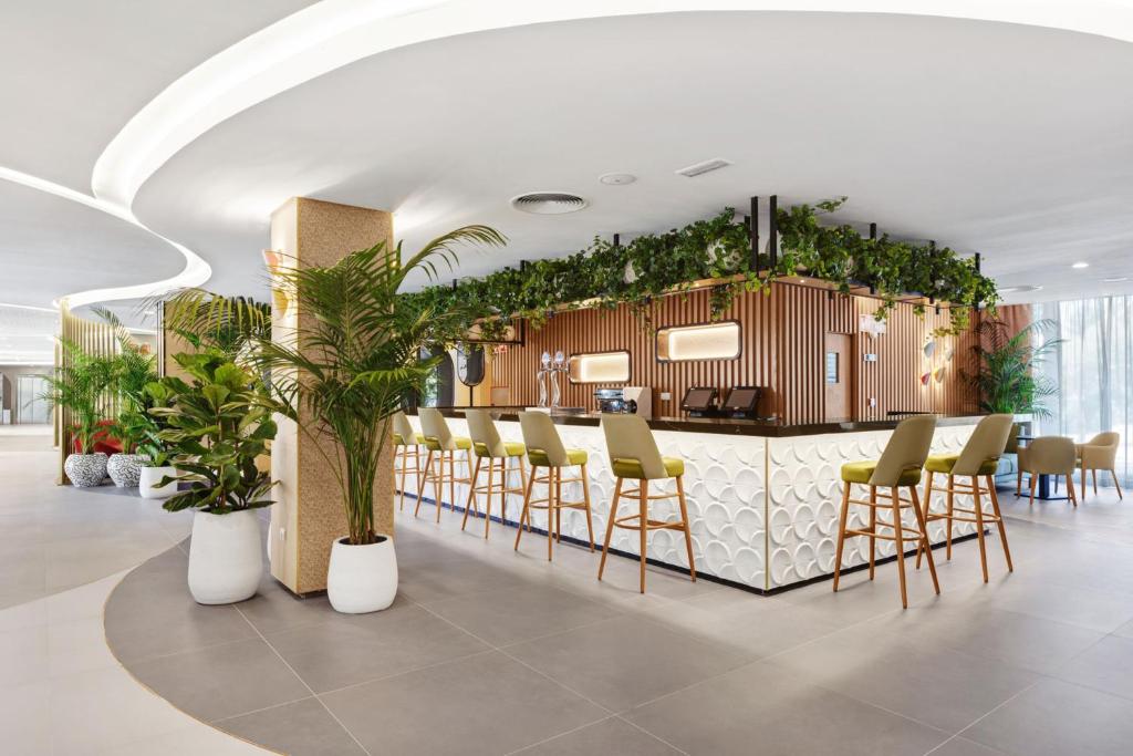 Mūsdienīgs viesnīcas bārs ar stilīgu interjeru, zaļām augu kompozīcijām un ērtām krēsliem. Gaisīga atmosfēra un dabas elementi rada relaksējošu vidi.