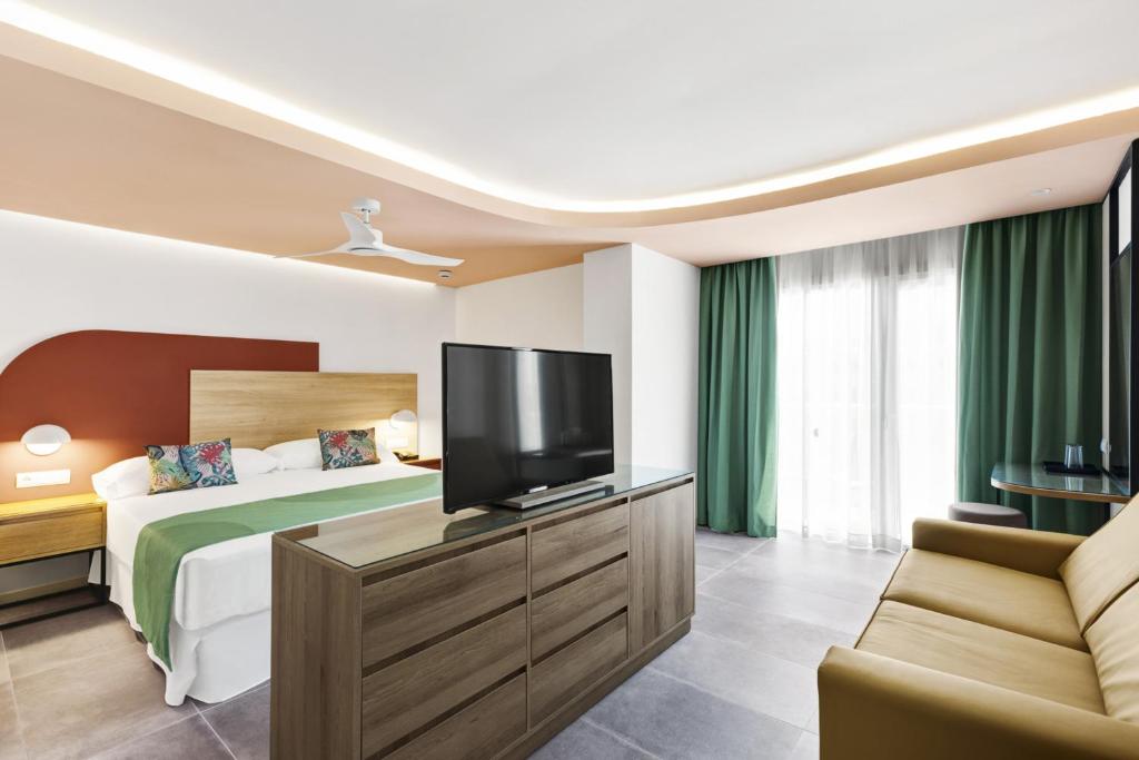 Mūsdienīgs viesnīcas numurs ar divguļamo gultu, televizoru un dīvānu. Interjers ir gaišs ar zaļiem aizkariem un koka mēbelēm.