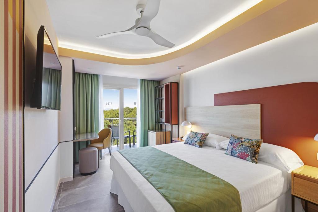 Mūsdienīga viesnīcas numura iekārtojums ar gaisīgu dizainu, zaļo gultas pārklāju un skatu uz terasi. Telpā ir televizors, galds un komfortabla krēsls.