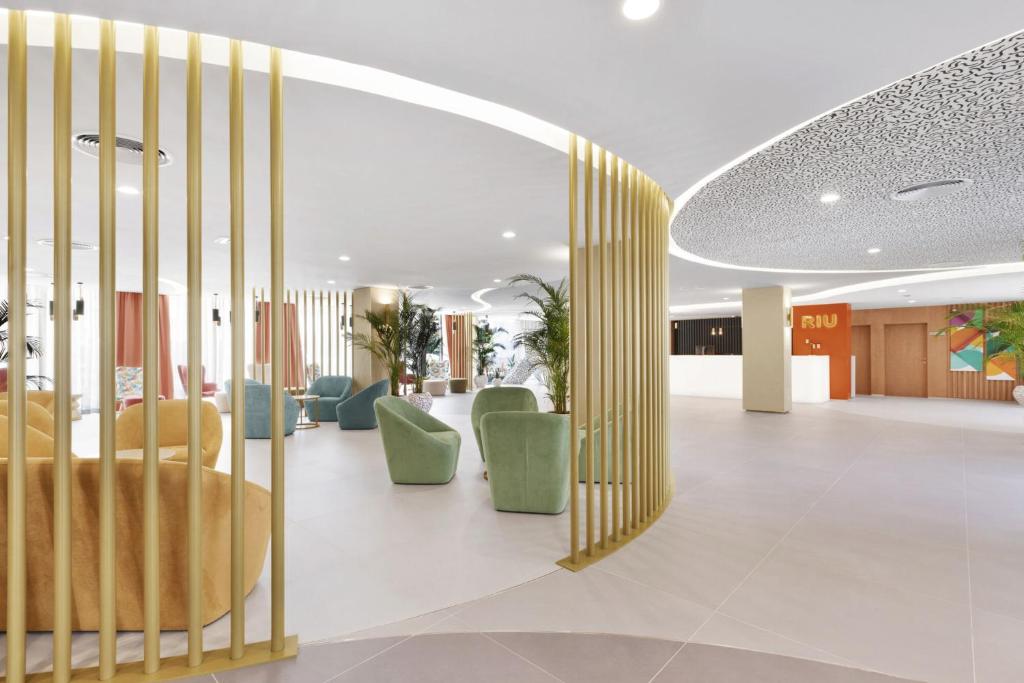 Mūsdienīgs viesnīcas interjers ar stilīgu dizainu, iekļaujot krāsainus krēslus un dekoratīvas augu kompozīcijas. Viegli apgaismotā telpa rada patīkamu atmosfēru.