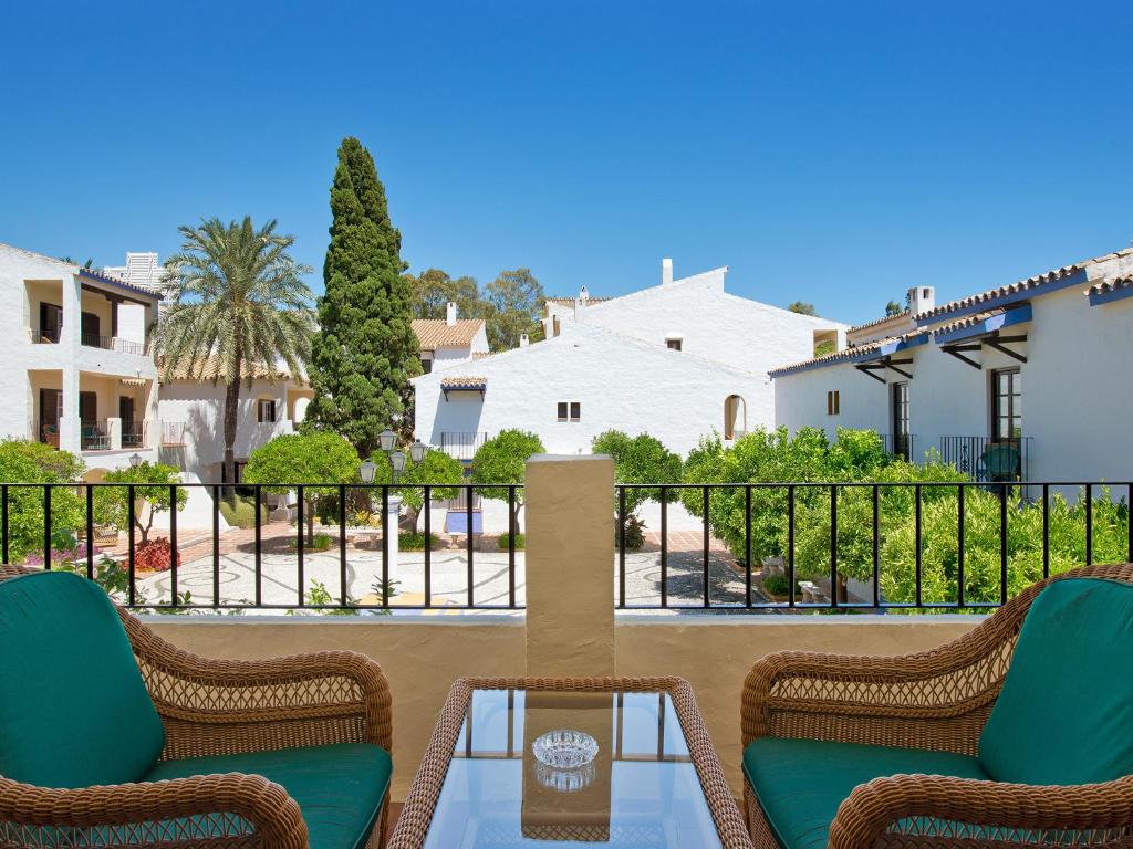 Skats no balkona uz gleznainu pagalmu ar palmām un baltiem māju fasādēm, kas rada mierīgu atmosfēru.