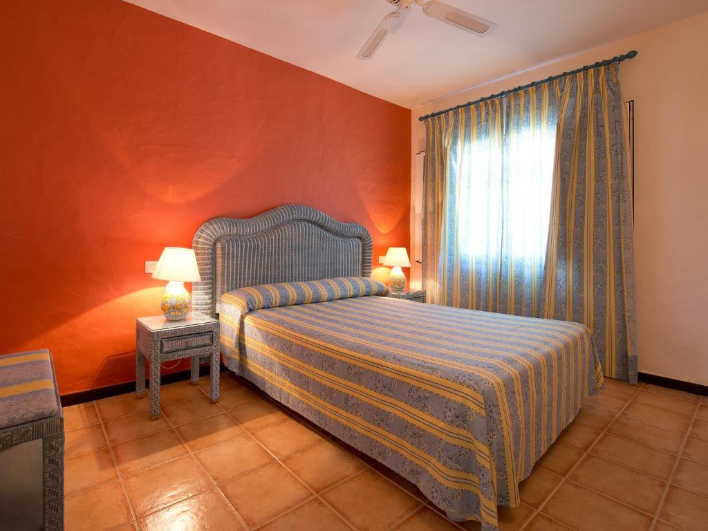 Mūsdienīga guļamistaba ar stilīgu gultu un krāsainu sienu, papildināta ar gaismas lampām un aizkariem. Siltas krāsas un ērtas mēbeles veido patīkamu atmosfēru.