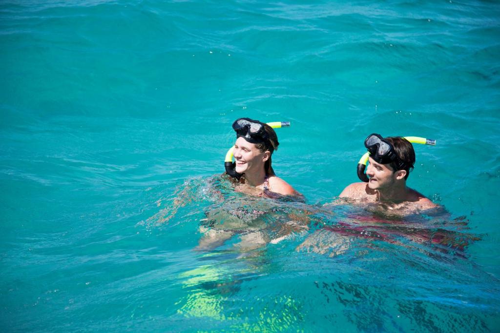 Divi cilvēki ar snorkeli, kas priecīgi peld ūdenī. Skats uz tīru, zilganu ūdeni, kurā viņi izbauda ūdens aktivitātes.