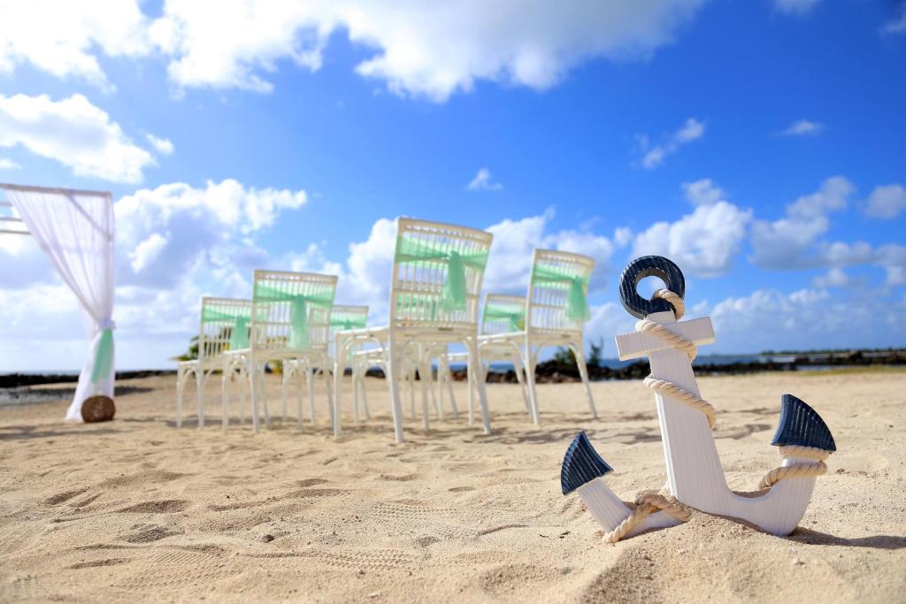 Pludmales kāzu dekorācijas ar baltu ankeru un krēslu rindu zem skaidras debesis.