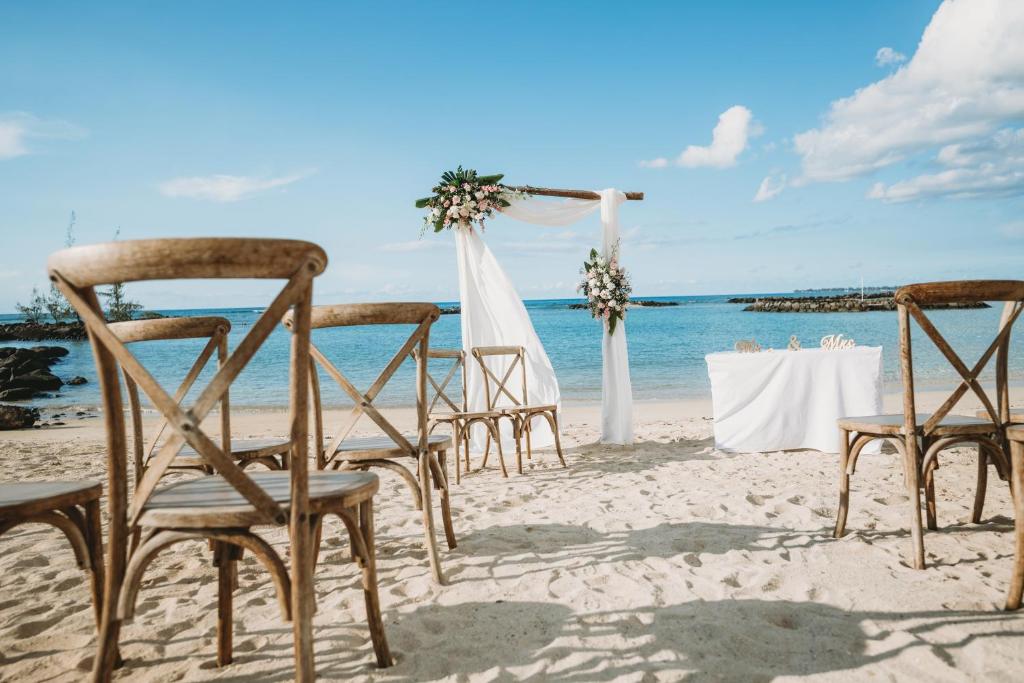 Pludmales kāzu ceremonija ar koka krēsliem un dekorētu altāri, fonā redzams jūra un debesis.