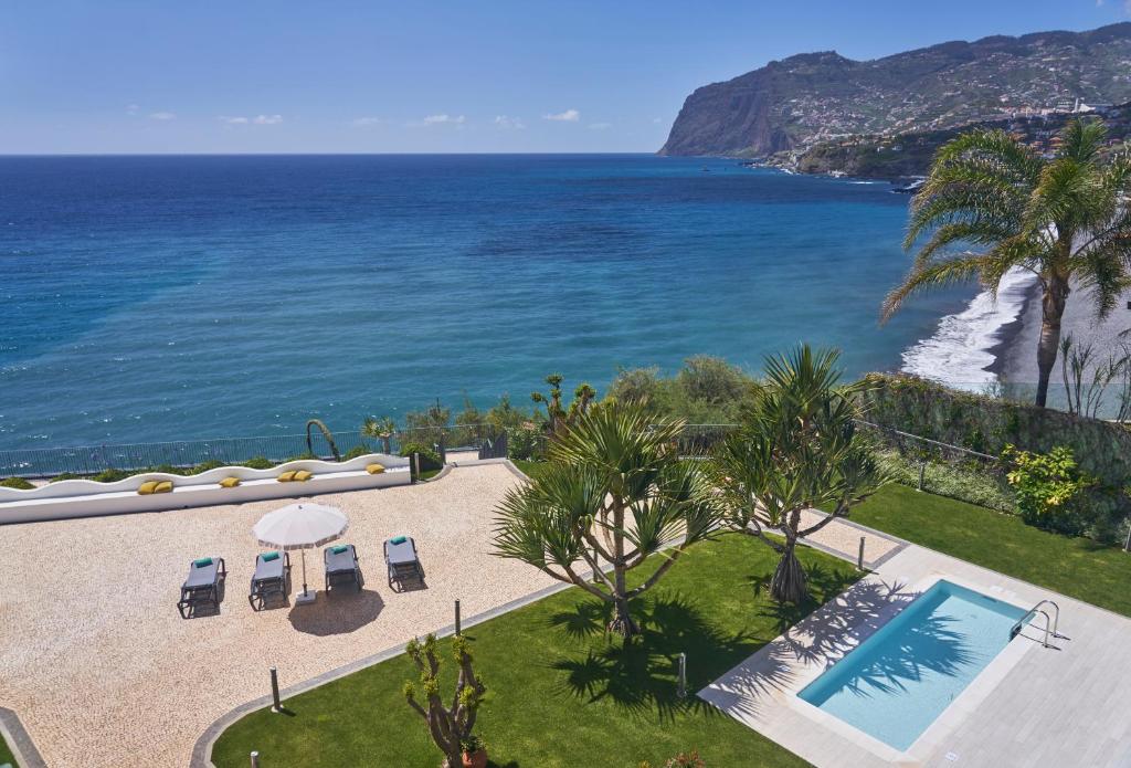 Viesmīlīgs skats uz jūru ar peldbaseinu un saulē sildāmām atpūtas krēslām, apzaļumojums un pludmale fona.