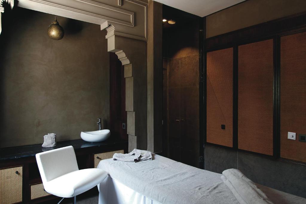 Relaksējoša spa telpa ar minimālistisku dizainu, gaišu krēslu un masāžas galdu. Sienas ir krāsotas neitrālās krāsās, radot mierīgu atmosfēru.