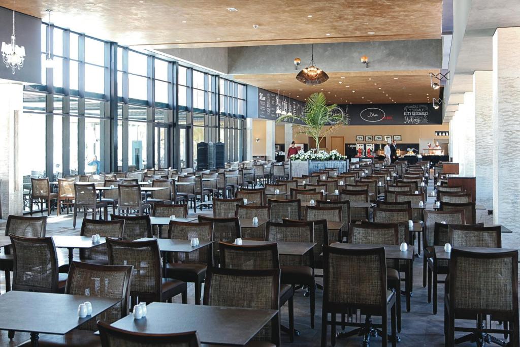 Liela un moderna restorāna telpa ar daudzām koka galdiem un krēsliem. Labi apgaismota vide, kas satur lielus logus un zaļu augu dekorāciju.