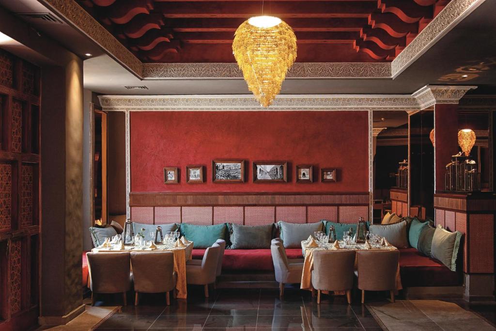 Elegants restorāns ar siltu sarkanu sienu, grezniem gaismas ķermeņiem un ērtām sēdvietām, kas rada patīkamu atmosfēru. Interjers ietver izsmalcinātus dekora elementus un vintage fotogrāfijas.