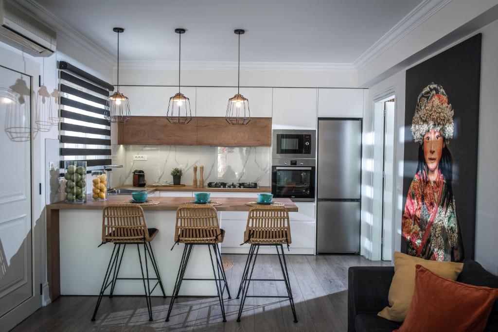 Mūsdienīga virtuve ar koka akcentiem, stilīgiem gaismas ķermeņiem un ērtām krēslām pie galda, kas rotāta ar augļu traukiem un mākslinieciskiem elementiem.