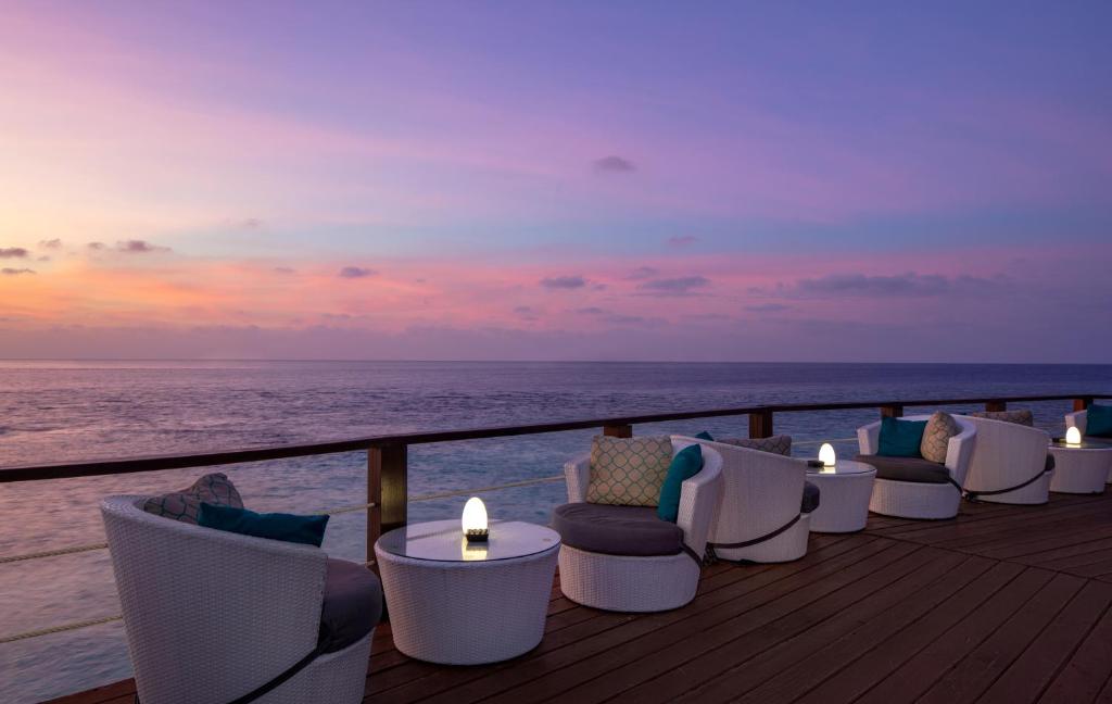 Mūsdienīgs terases interjers ar ērtām baltām mēbelēm, kas piedāvā skatu uz saulrietu virs okeāna. Gaismas elementi uz galdiem rada patīkamu atmosfēru.