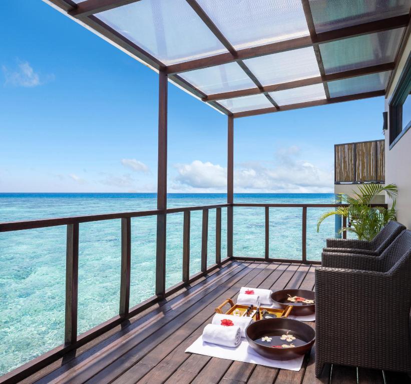 Lieliska terase ar skatu uz kristāldzidru ūdeni, kurā redzami divi ērti krēsli un dekoratīvas bļodas ar ziediem. Ideāla vieta relaksācijai un atpūtai pie jūras.