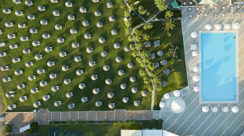 Vasaras kūrortā redzama plaša peldbaseina zona ar saulessargiem un atpūtas krēsliem, kas izkārtoti uz zaļās zāles. Ideāla vieta relaksācijai un izklaidei.