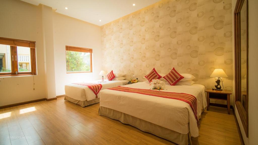 Mūsdienīga viesnīcas numura interjers ar divām gultām, koka grīdu un logiem, caur kuriem plūst dabiska gaisma. Uz gultām ir spilveni ar sarkaniem akcentiem un dekoratīvi ziedi uz gultas.