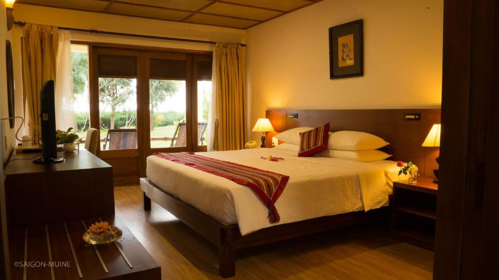 Mūsdienīga viesnīcas numuriņa interjers ar divguļamo gultu, koka mēbelēm un logiem, kas ved uz dārzu. Numuriņā ir televizors un apgaismojums, kas rada siltu atmosfēru.