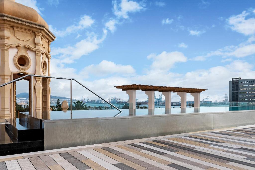 Mūsdienīgs terases skats ar arhitektūras elementiem un ainavu, kas ietver ostu un debesu zilu fonu. Ideāla vieta relaksācijai un atpūtai.