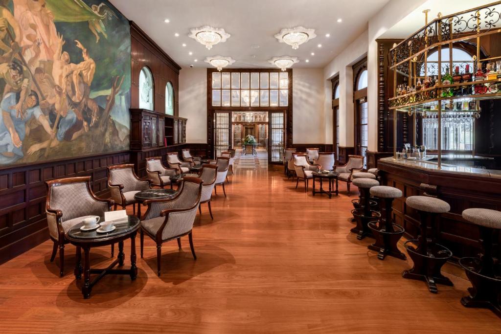 Elegants interjers ar māksliniecisku gleznu uz sienas, ērtiem krēsliem un bāru. Koka grīda un lieli logi nodrošina gaismas plūsmu.