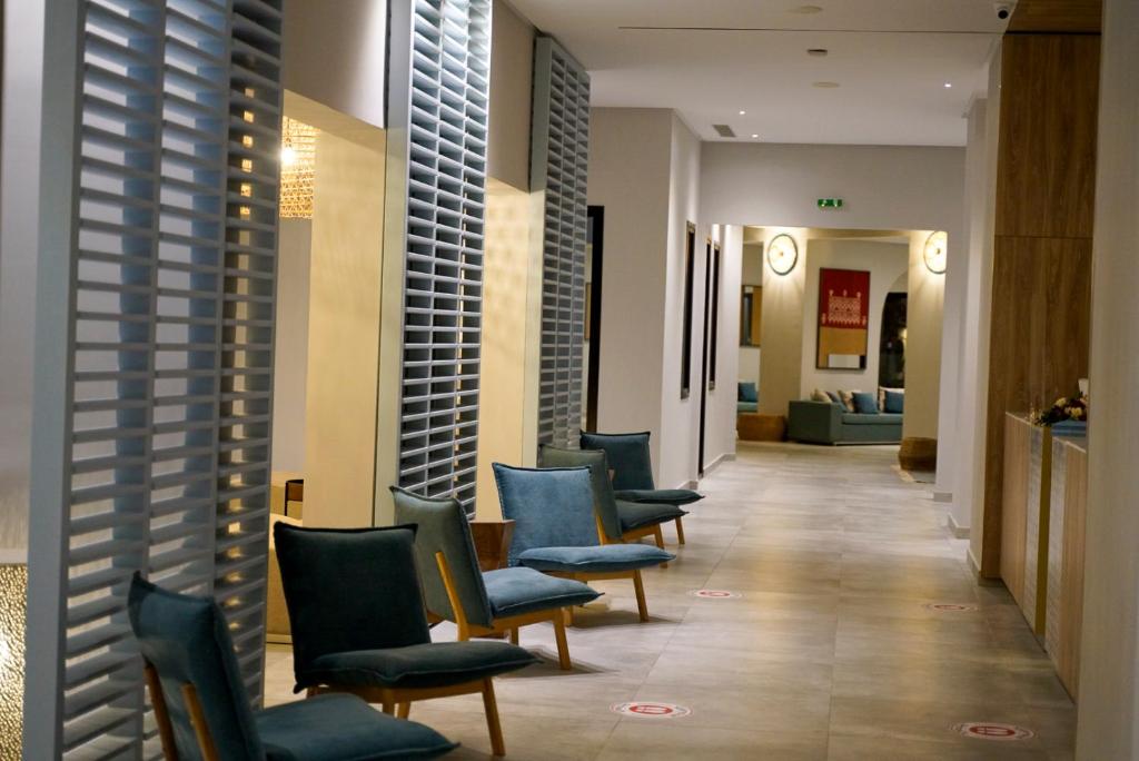 Mūsdienīga viesnīcas gaiteņa aina ar elegantām zālītes krēslām un izsmalcinātu apgaismojumu. Gaiteņa malās redzami mākslas darbi un relaksējošas zonas.