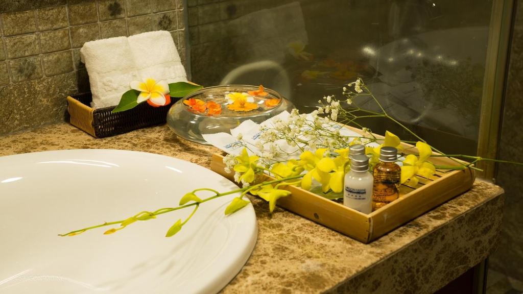 Vannas istabas stilizēts interjers ar dvieļiem, ziediem un higiēnas līdzekļiem, kas sakārtoti uz galda. Rūpīgi izvēlēti dekori rada relaksējošu atmosfēru.