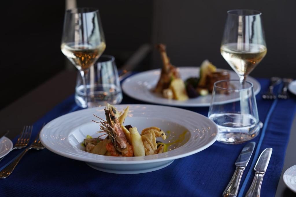 Elegants vakariņu galds ar gourmet ēdieniem un baltu vīnu, izcelti garneles un dārzeņu porcijas. Ideāla atmosfēra, lai izbaudītu kulinārijas priekus.