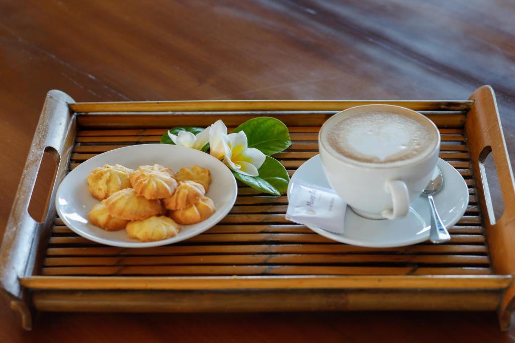 Kafijas tasīte ar putotu pienu un maziem cepumiem uz koka trauka, dekorēta ar ziedu un lapām.