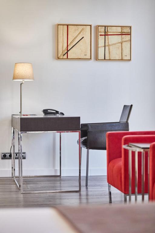 Mūsdienīgs birojs ar elegantu galdu, melnu krēslu un divām abstraktām gleznām uz sienas. Siltās gaismas lampas klātbūtne piešķir telpai mājīgumu.