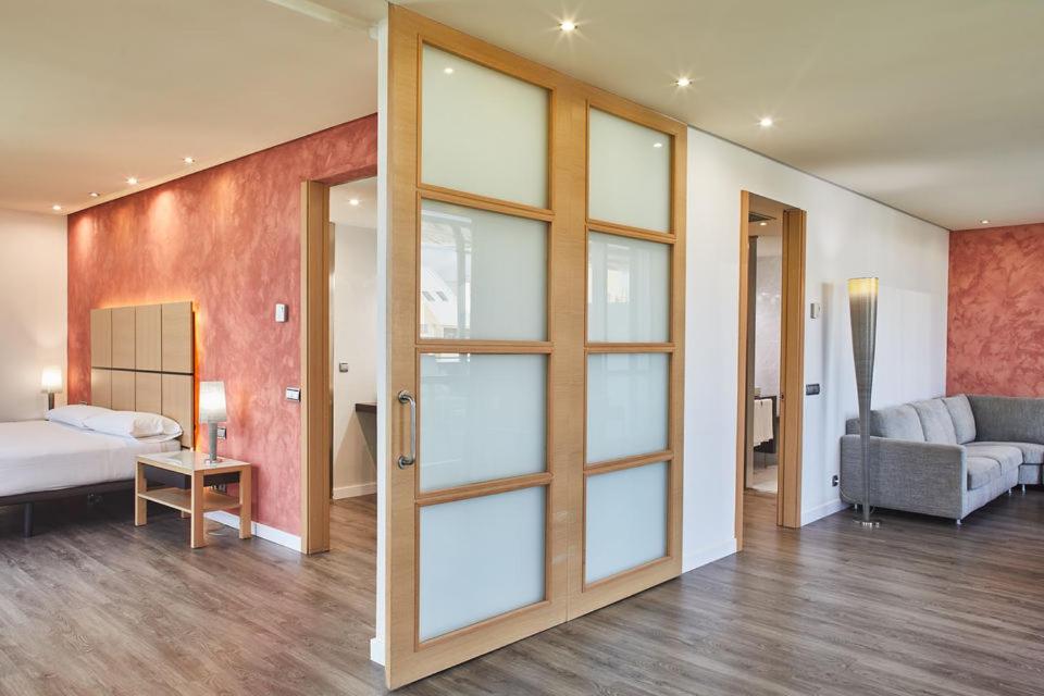 Mūsdienīga viesnīcas numura interjers ar koka durvīm, kuras atdala guļamistabu un viesistabu, gaišām sienām un modernu mēbelēšanu. Numurā ir ērta sofa un gaismas avoti, kas rada patīkamu atmosfēru.