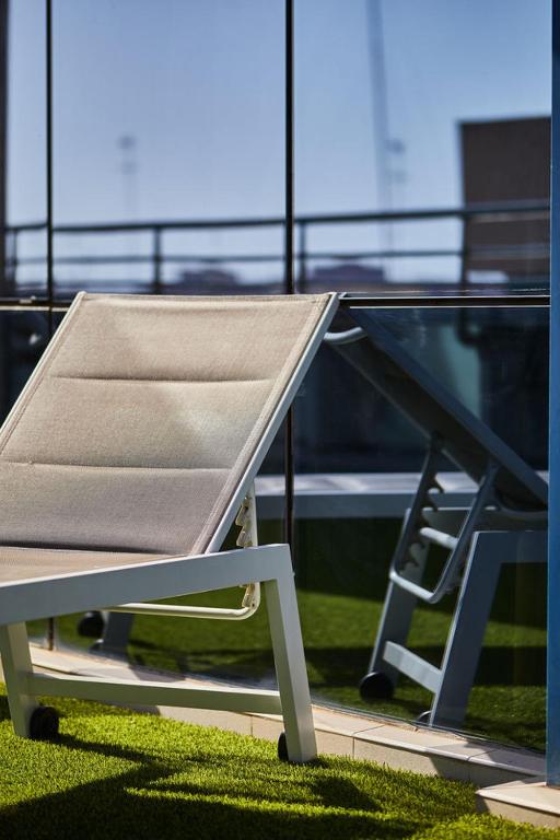 Saulaina terases atpūtas krēsls ar stikla sienu fona un zaļo zālienu. Ideāla vieta atpūtai un relaksācijai.