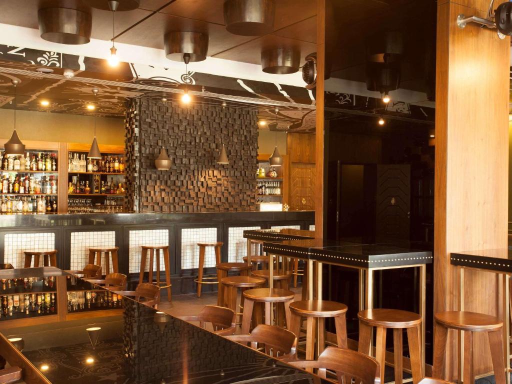 Mūsdienīgs bārs ar elegantu interjeru, kurā ir koka elementu un modernu apgaismojumu kombinācija. Bāra stūrī ir plaša alkoholisko dzērienu izvēle, savukārt pie galdiem ir koka krēsli, kas nodrošina ērtu sēdēšanu.