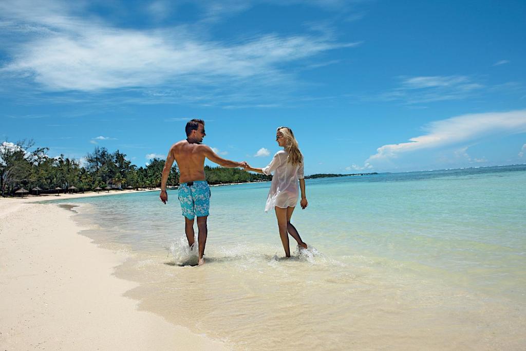 Pāris pastaigā pa pludmali saulainā dienā, izbaudot siltu ūdeni un romantisku atmosfēru. Skats uz dzidru jūru un debesīm ar mākonīšiem.