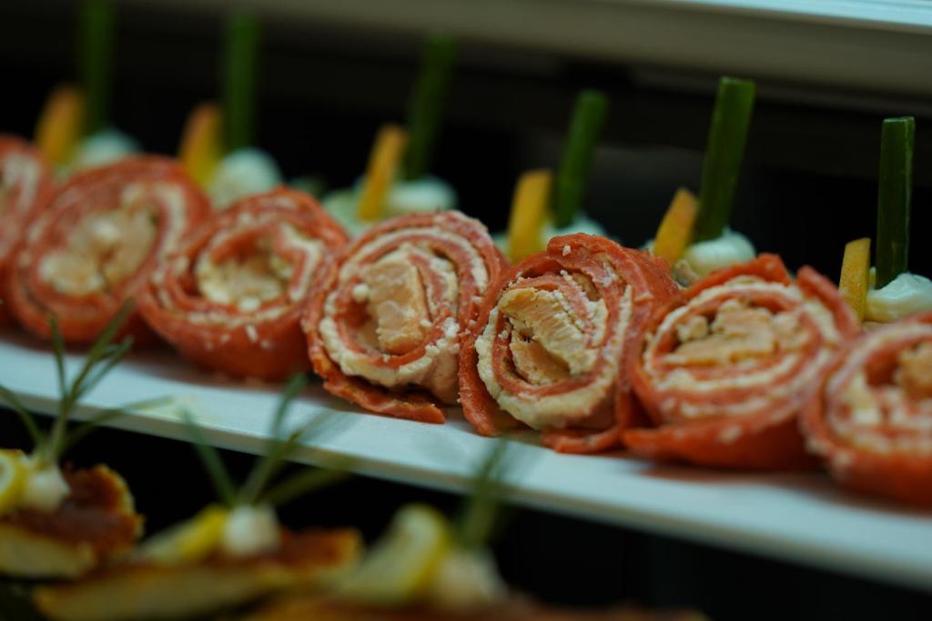 Svaigu un krāsainu sushi rullīšu šķīvis, kas satur zivju un krēmsiera pildījumu, rotāts ar dārzeņiem un garnelēm.