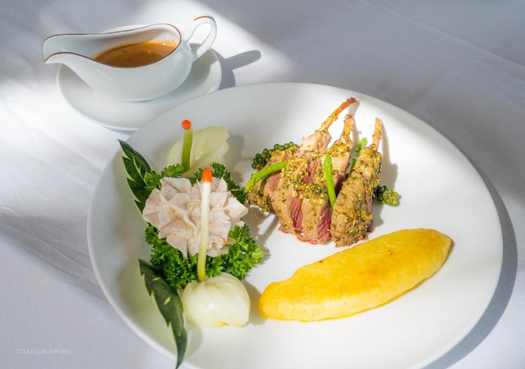 Garnēta gaļas šķēle ar dārzeņiem un mērci, pasniegta uz balta šķīvja. Svaigi zaļumi un krāsaini dārzeņi veido pievilcīgu kompozīciju.