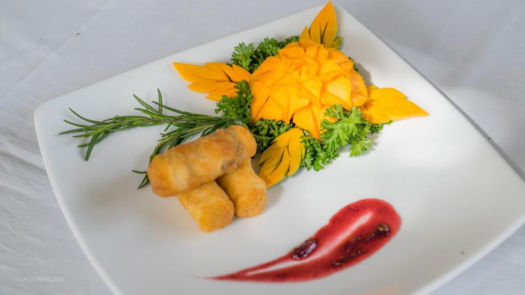 Plāksne ar stilizētu dārzeņu un augļu dekorāciju, ieskaitot mango ziedu un zaļumus, kā arī fritētu uzkodu. Garšīga un vizuāli pievilcīga maltīte.