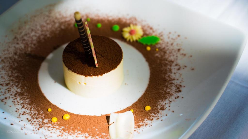 Elegants deserts ar krēmīgu tekstūru, pārklāts ar kakao pulveri un dekorēts ar šokolādes stienīšiem un krāsainām konfektēm. Ideāls piemērs mūsdienu kulinārijas mākslai.