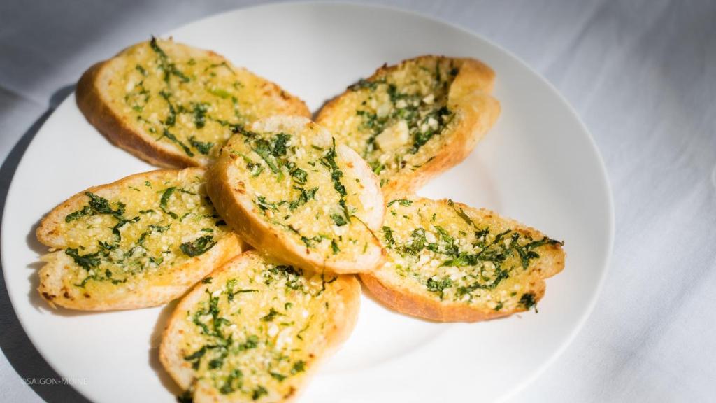 Kārtainā maizīte ar garšaugiem un sieru, izkārtota uz balta šķīvja, piedāvā gardu uzkodu. Ideāla izvēle, lai baudītu kopā ar draugiem vai kā piedevu maltītēm.