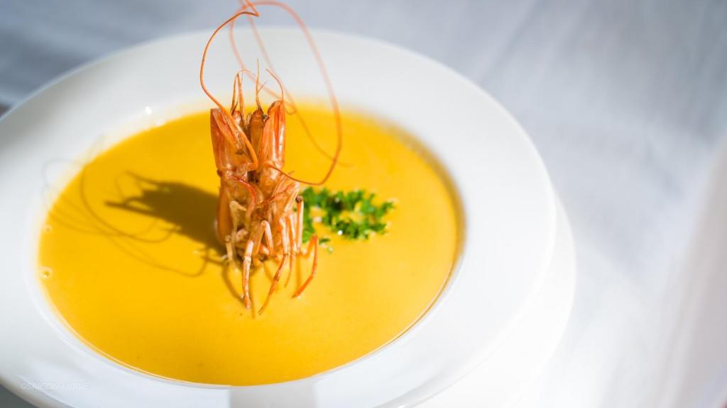 Zivju zupa ar garnelēm, dekorēta ar zaļumiem, pasniegta baltā šķīvī.