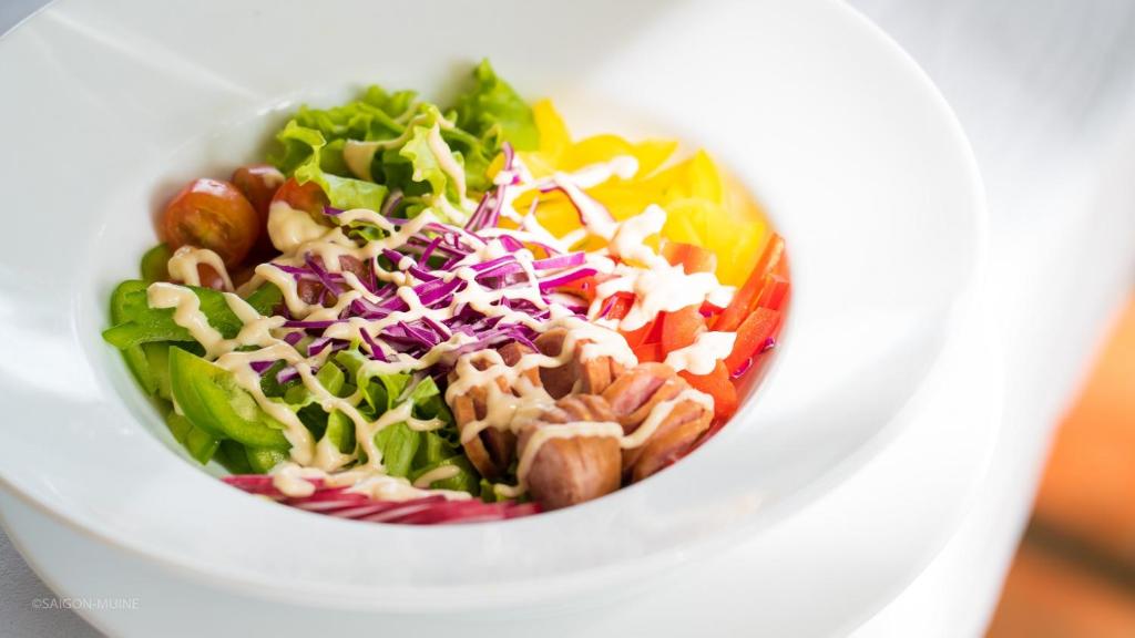 Svaiga un krāsaina salātu bļoda ar dažādiem dārzeņiem, ieskaitot salātlapas, tomātus un papriku, rotāta ar krēmīgu mērci.