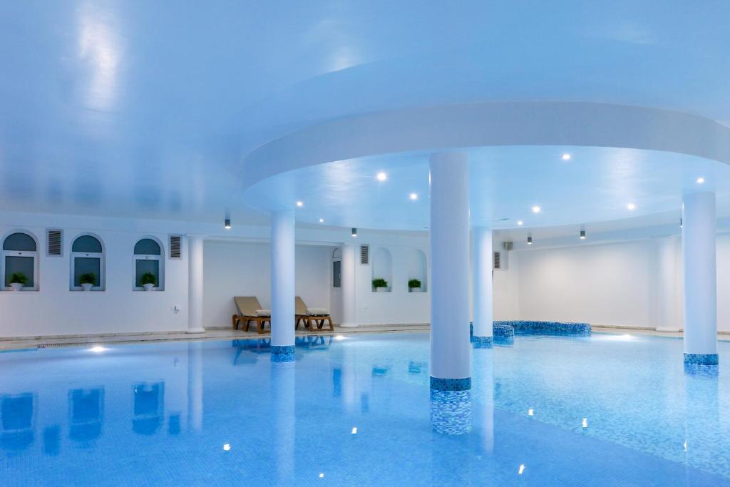 Mūsdienīgs iekštelpu baseins ar zilu ūdeni, apgaismots ar siltām gaismām un elegantām kolonnām. Telpa ir gaiša un relaksējoša, piedāvājot mierīgu atmosfēru.