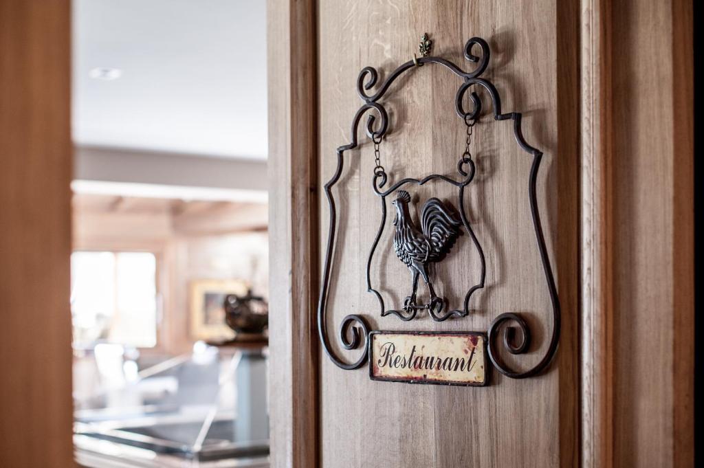 Kādu dekoratīvu metāla zīmi ar vārdu "Restorāns", kas ir piestiprināta pie koka sienas, ar vistas attēlu. Zīme piešķir mājīgu atmosfēru un norāda uz ēdināšanas vietu.